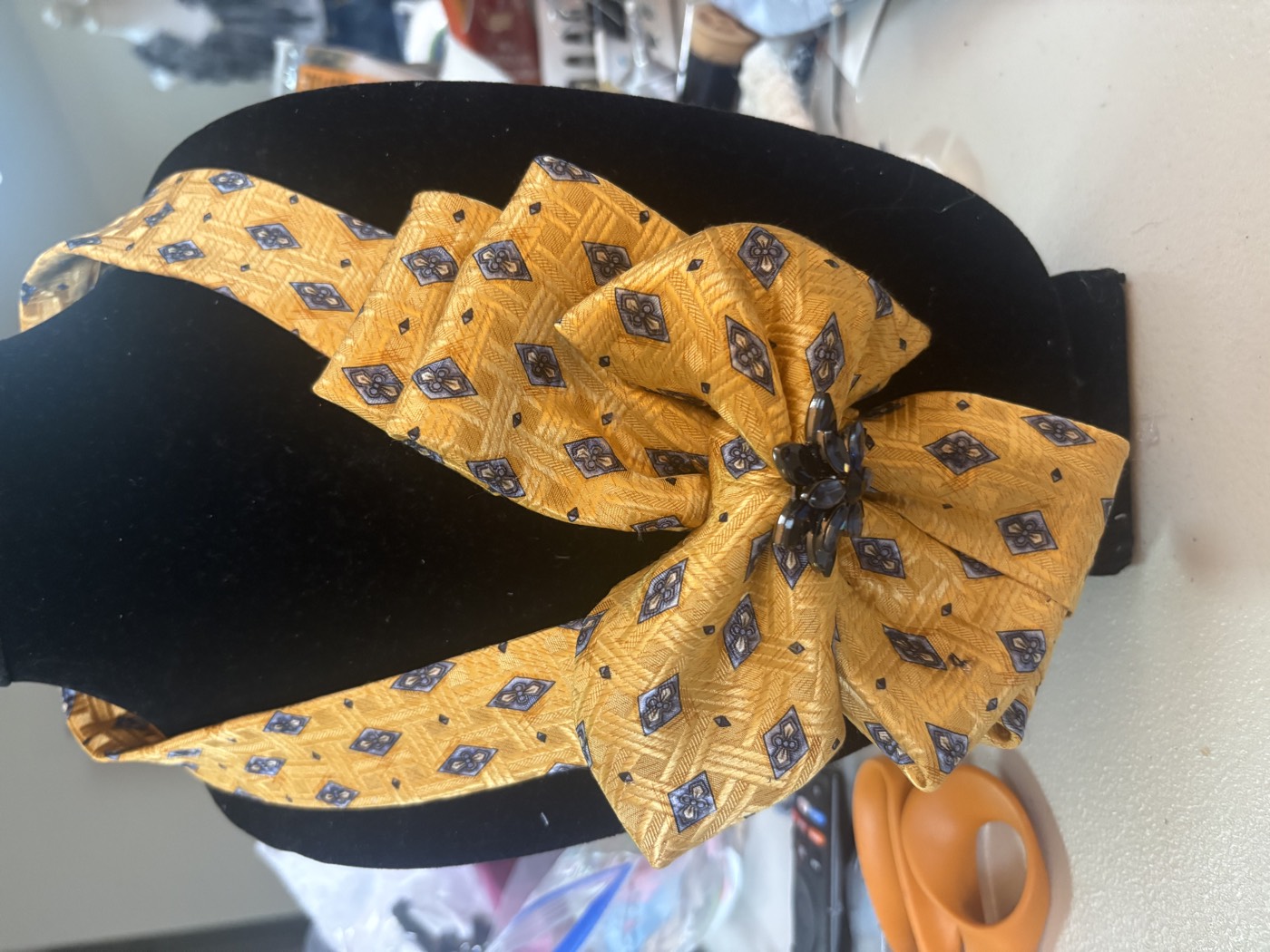 Gold and navy patterned necktie folded into a bow-shaped necklace with a dark beaded center.
