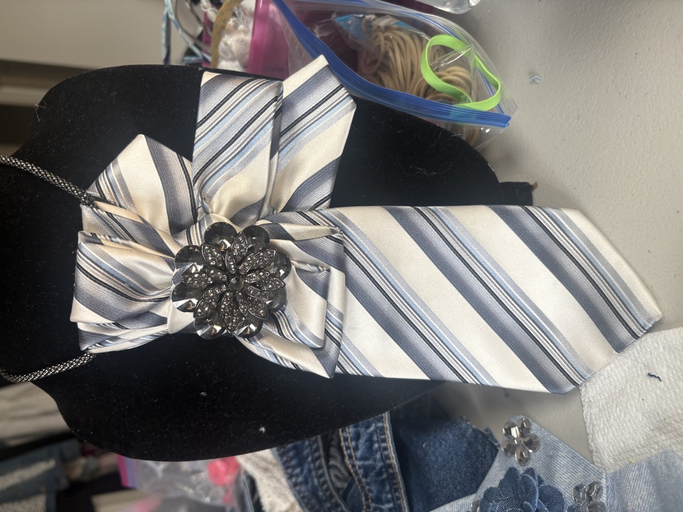 Cream and navy striped necktie gathered into a rosette with a pewter flower brooch, on a chain.