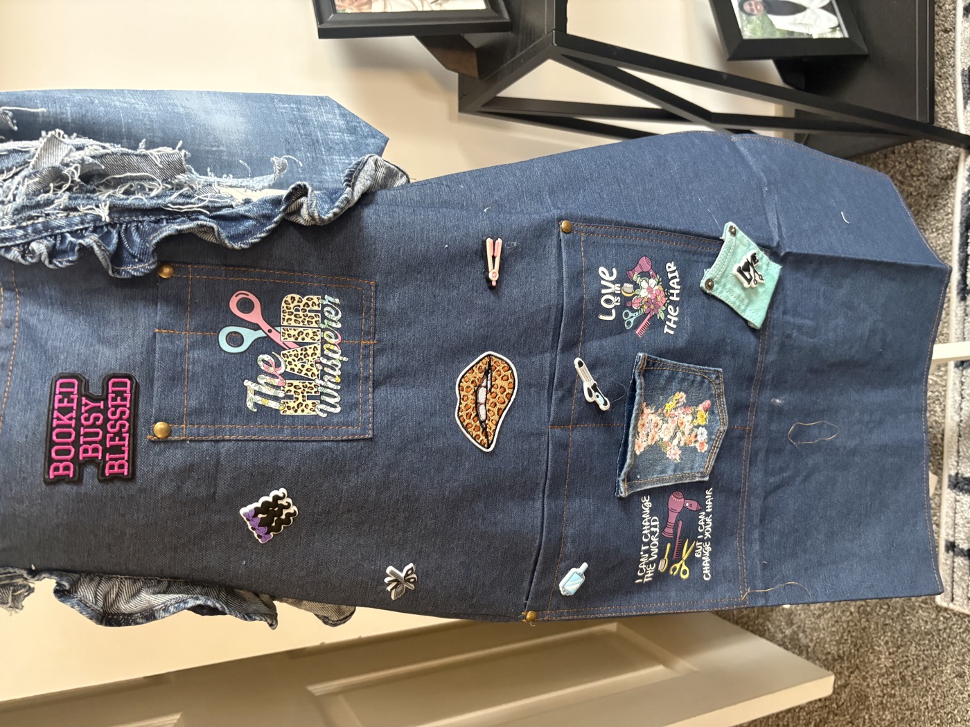 Denim apron covered in patches: Booked Busy Blessed, The Hair Whisperer, scissors, lips and a small pocket.
