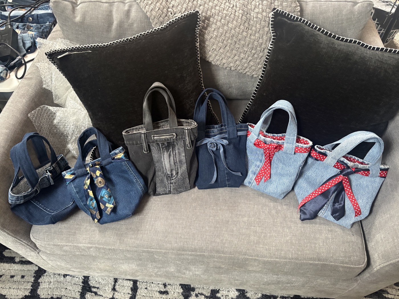 A row of small denim mini totes with ribbon bows and contrast linings on a couch.