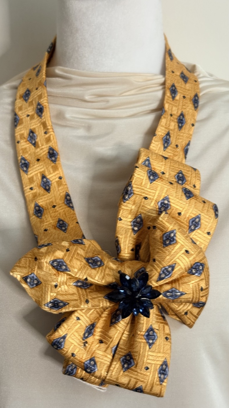 Marigold yellow necktie with navy diamonds, folded into a wide layered bow with a dark blue crystal flower at the center.