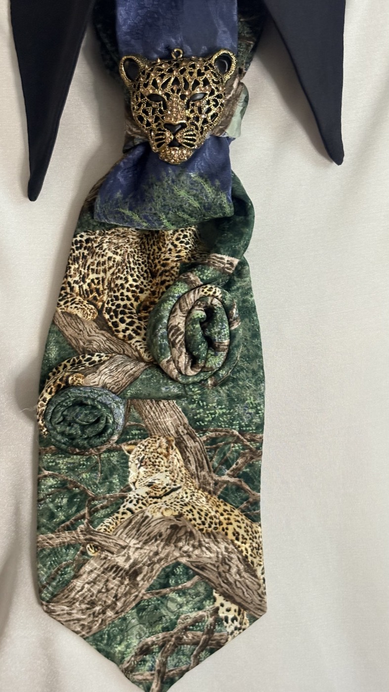 Green jungle-print necktie with leopards, gathered under a dark blue tie, finished with a brass leopard-head brooch.