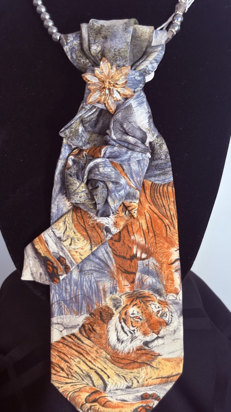 Tiger-print necktie in orange and blue-grey, gathered at the top with a small copper flower brooch, on a beaded chain.