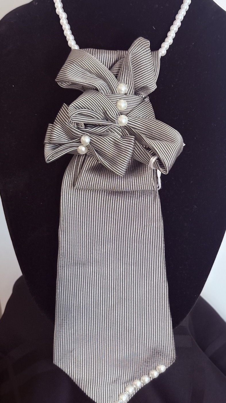 Silver-grey ribbed necktie folded into a triple bow with small pearls, on a pearl strand.