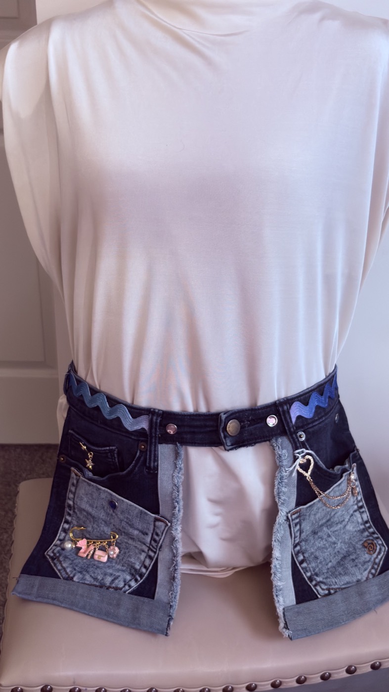 A pocket belt made from the waistband and front pockets of jeans, with rickrack trim and charms, worn on a mannequin.